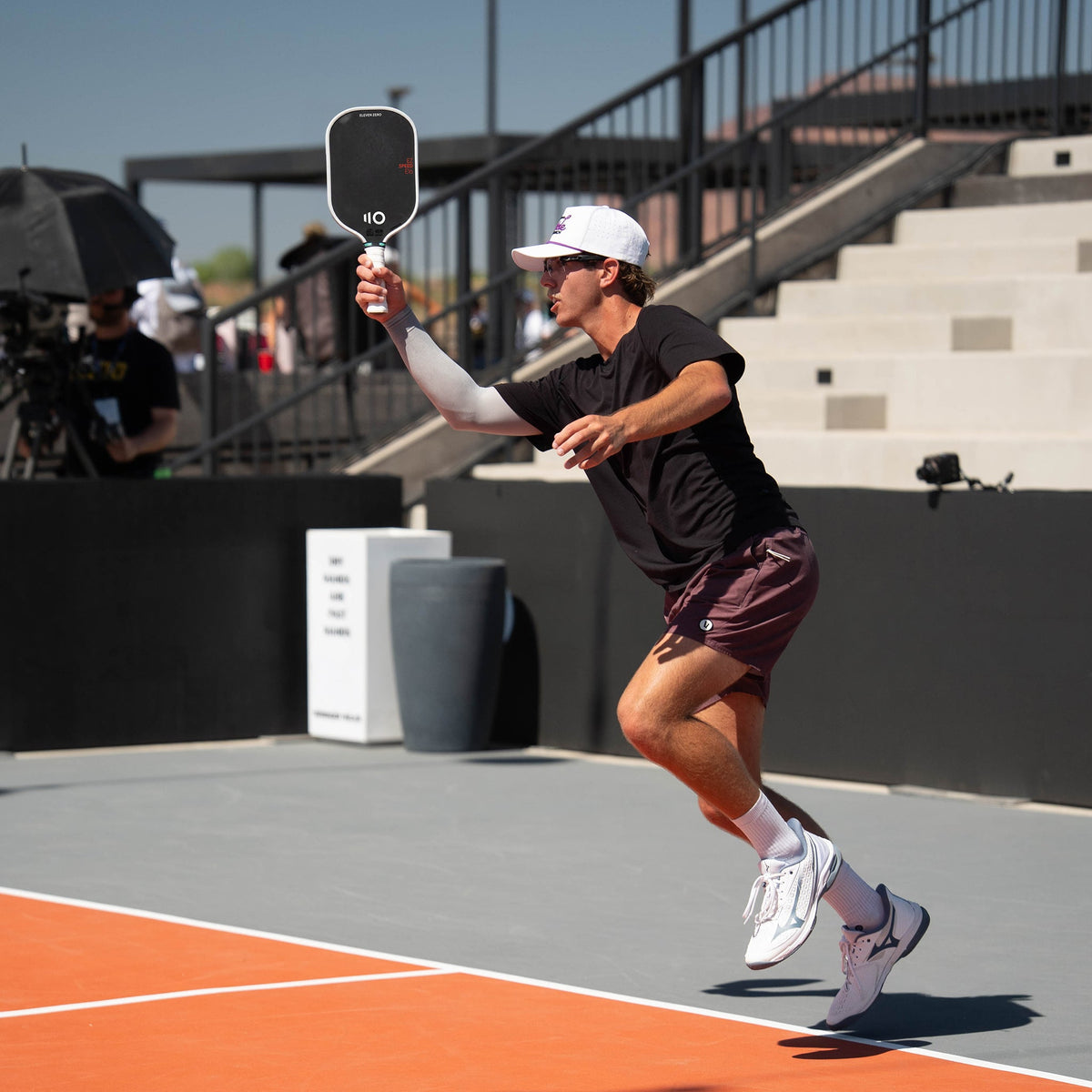 Pickleball player mid-swing at an outdoor tournament court holding an Eleven Zero EZ Speed paddle