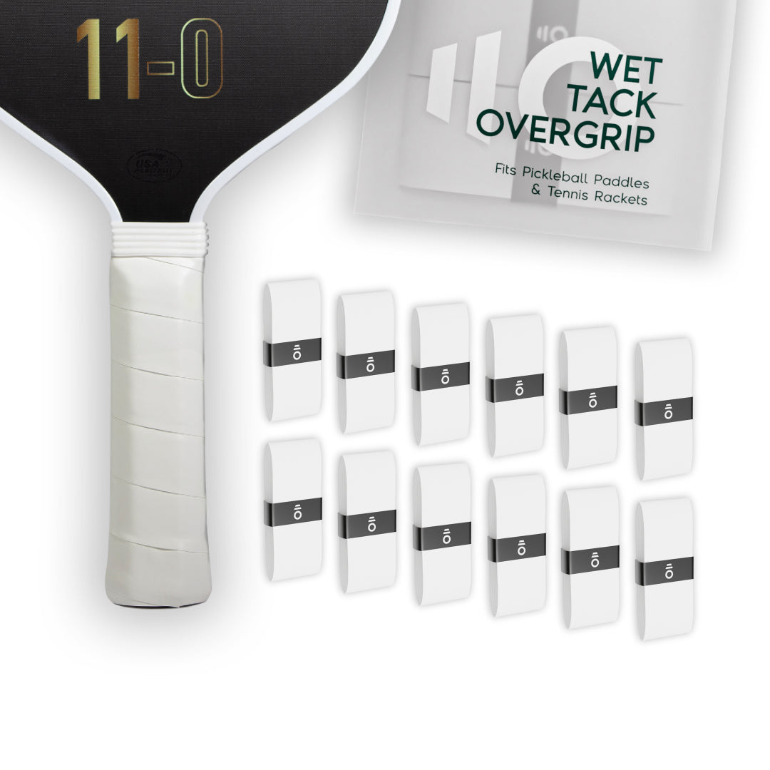 Twelve white Eleven Zero Wet Tack Overgrip strips arranged in rows beside the paddle handle and product packaging.