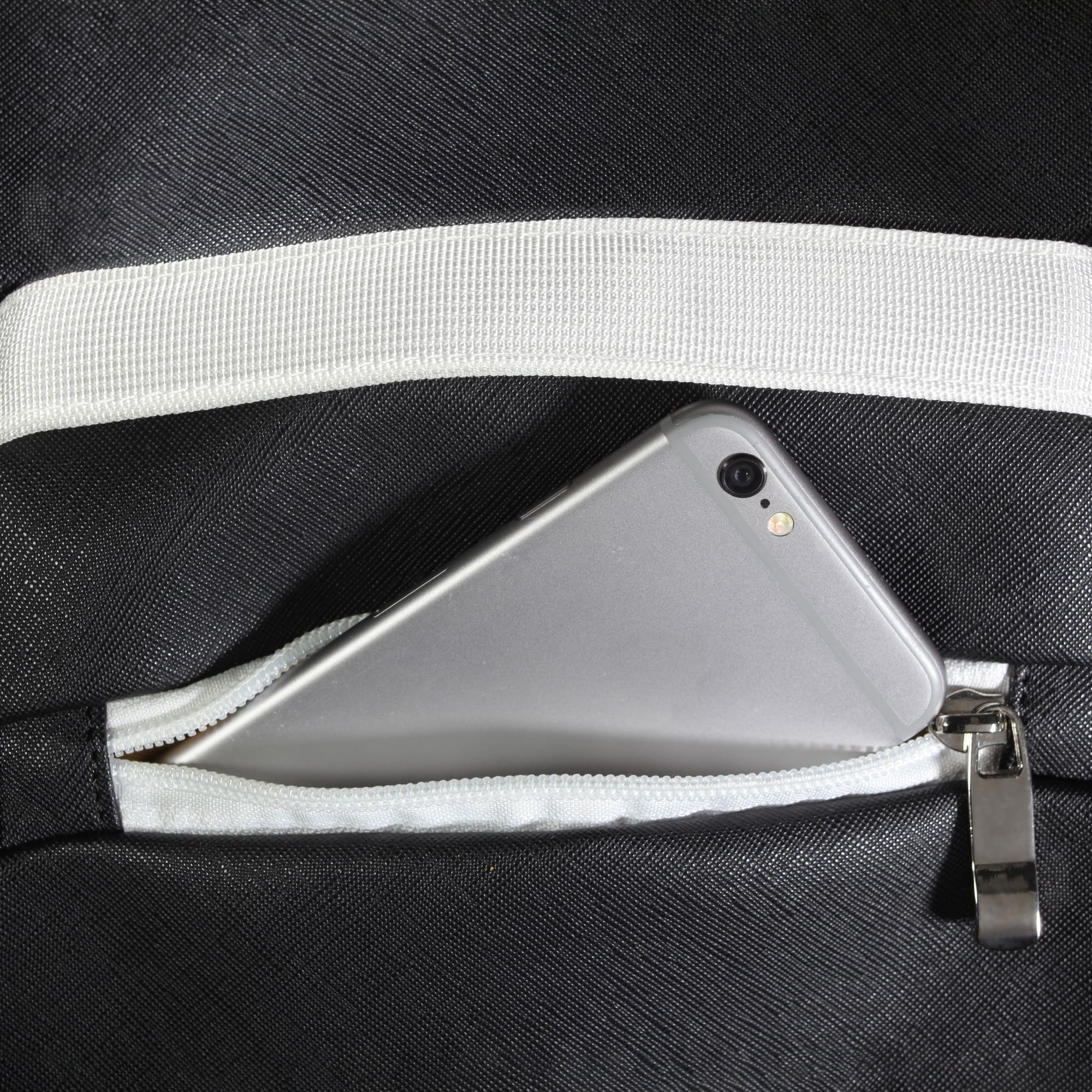 Close-up of zippered pocket on black Eleven Zero backpack with smartphone partially inside.