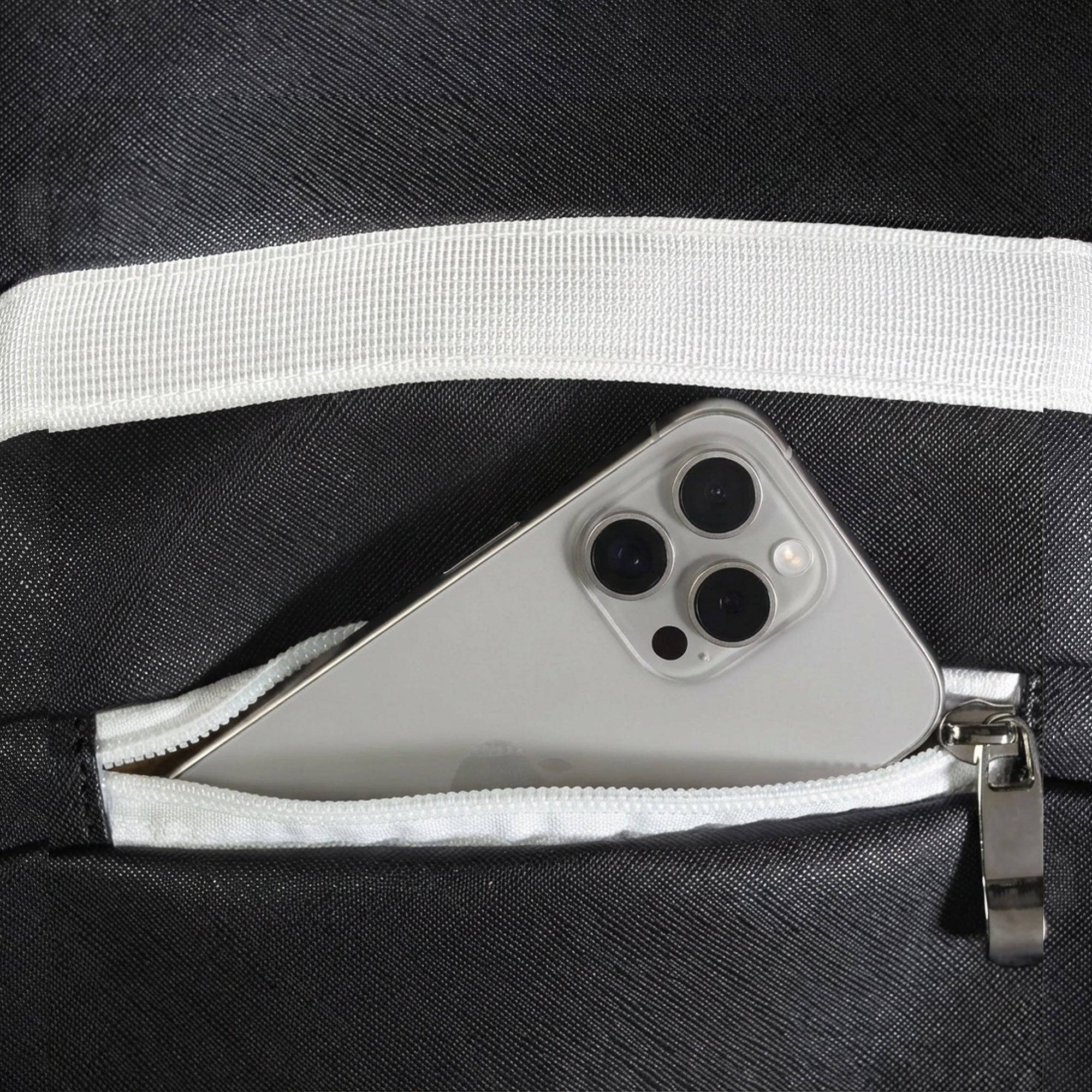 Close-up of zippered pocket on black Eleven Zero backpack with smartphone partially inside.