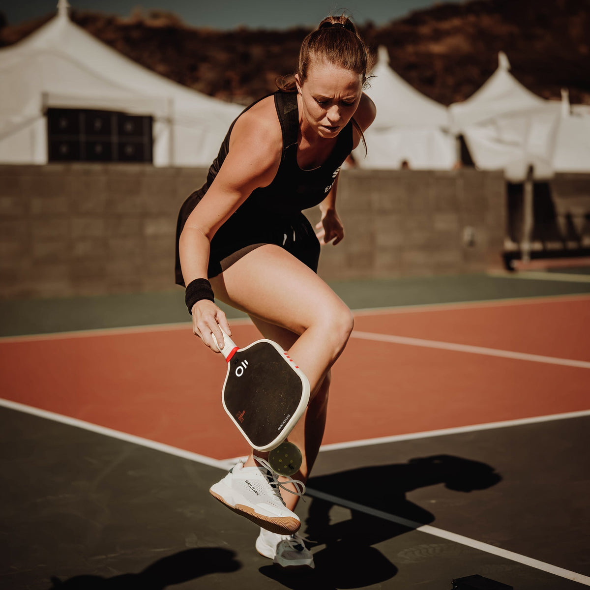 Pickleball player picking up a low ball with an Eleven Zero paddle on a red court