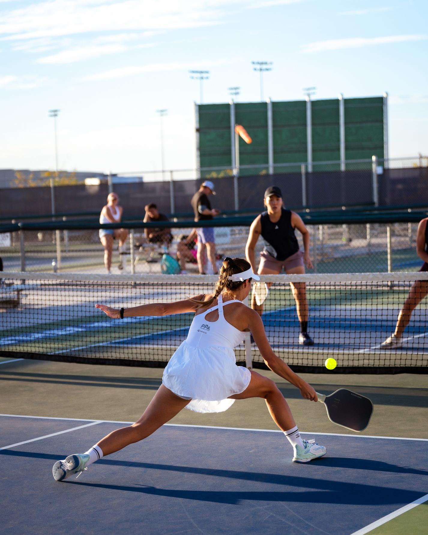 Pickleball player stretching for a low shot at the net during evening open play