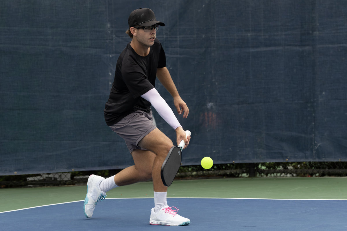 Pickleball player hitting a low ball with a black Eleven Zero E16 paddle on an outdoor court