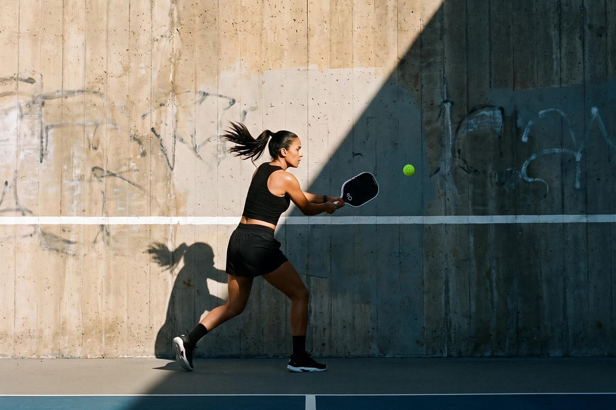 Pickleball player in black hitting a forehand against a concrete practice wall with an Eleven Zero paddle