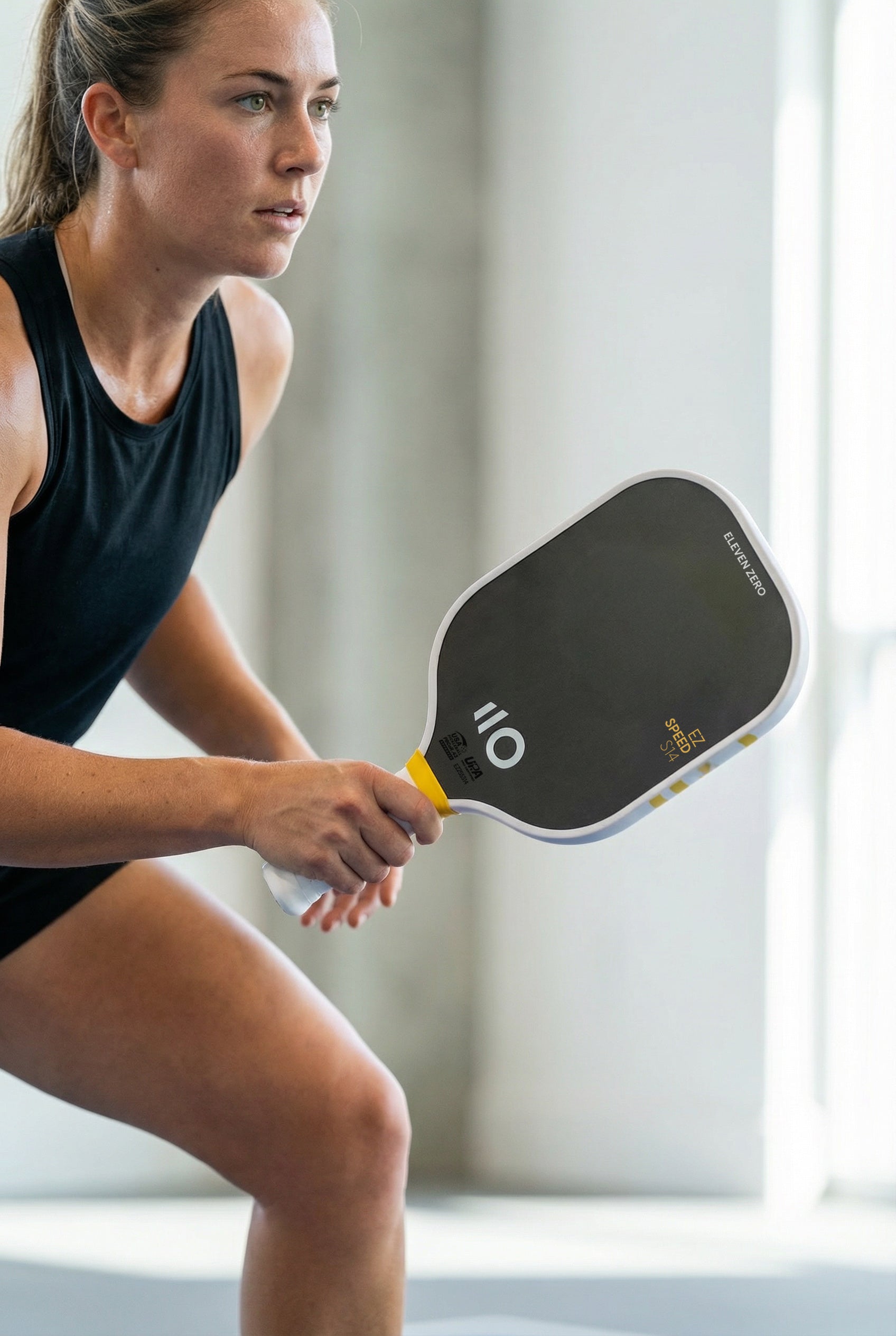 Focused pickleball player in ready position holding an Eleven Zero EZ Speed paddle