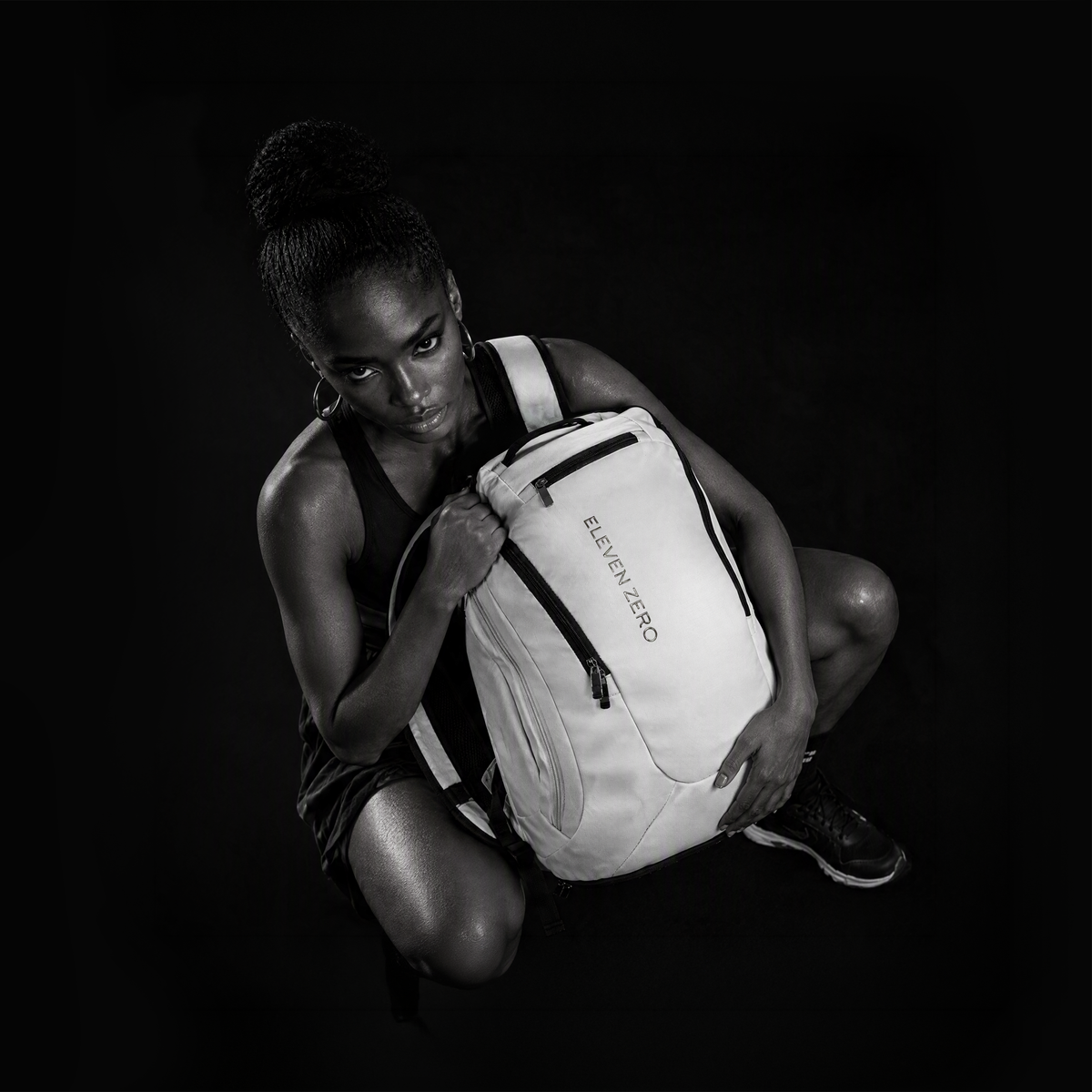a sportive woman sits on the ground and holds the Eleven Zero White Pickleball backpack which is 28 liters.