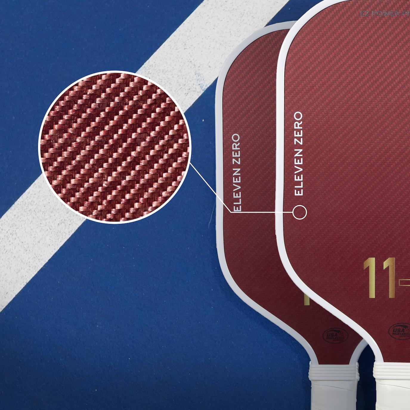 Close-up showing detailed texture of the maroon Aramid Carbon surface on Eleven Zero pickleball paddles, enhancing comfort and vibration dampening.