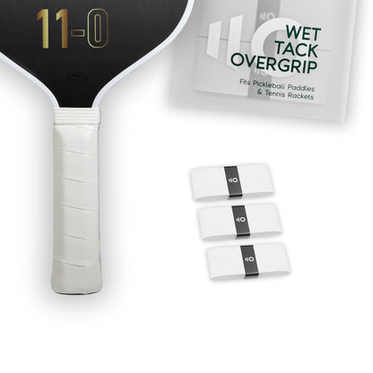 Three white Eleven Zero Wet Tack Overgrip strips shown beside the paddle handle and product packaging.