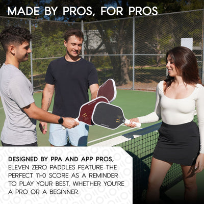 Three pickleball players smiling and touching Eleven Zero paddles—two maroon K-16 paddles and one black paddle—on a sunny outdoor pickleball court, illustrating paddles designed by professional players for both beginners and pros.