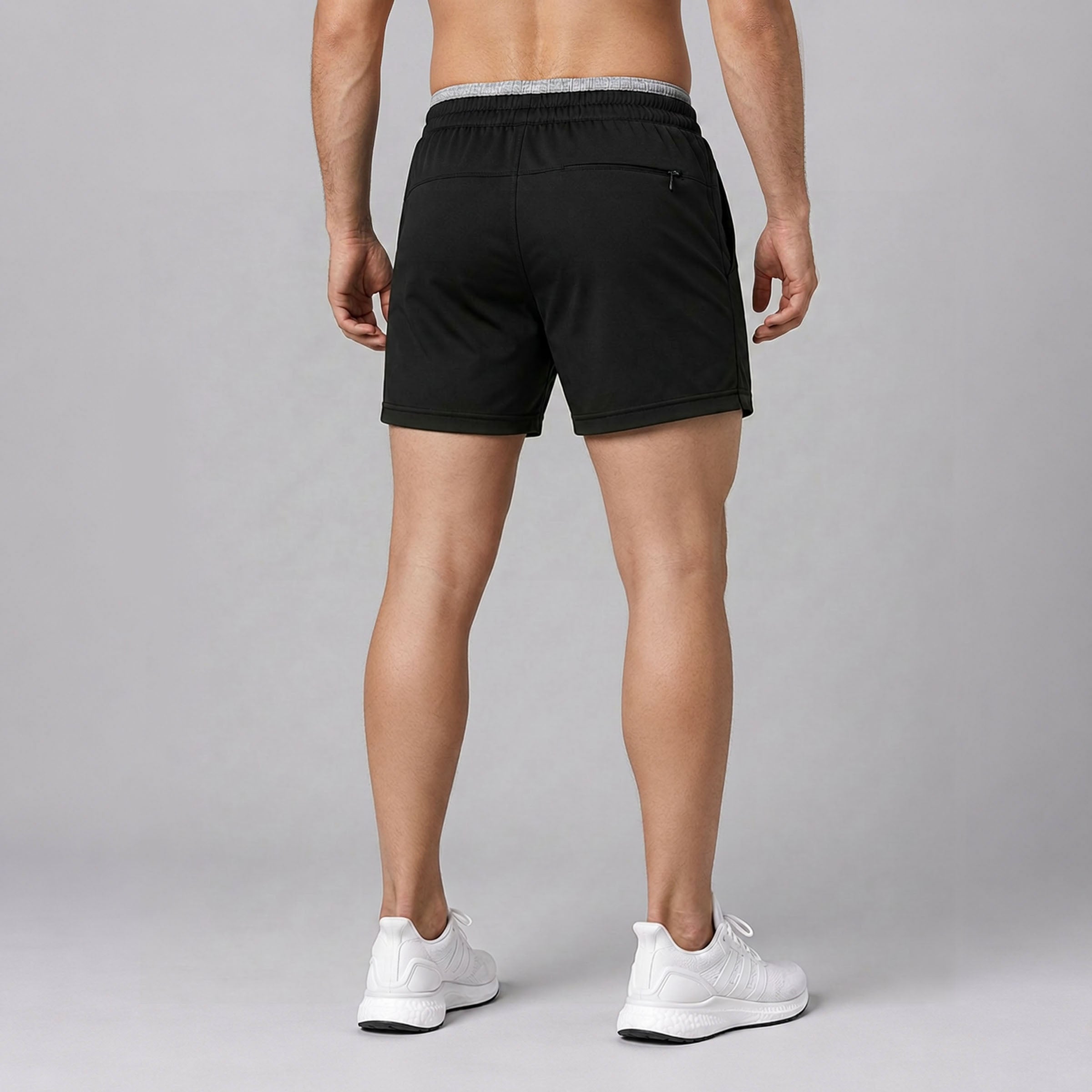 Person wearing black shorts and white sneakers on a gray background