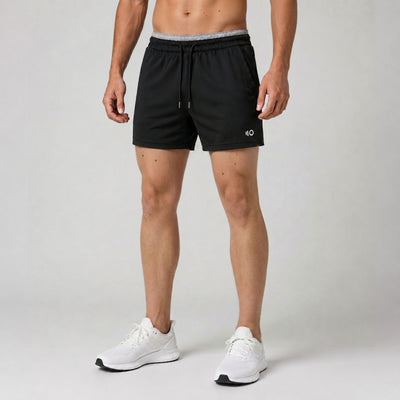 Person wearing black athletic shorts with a brand logo on a gray background