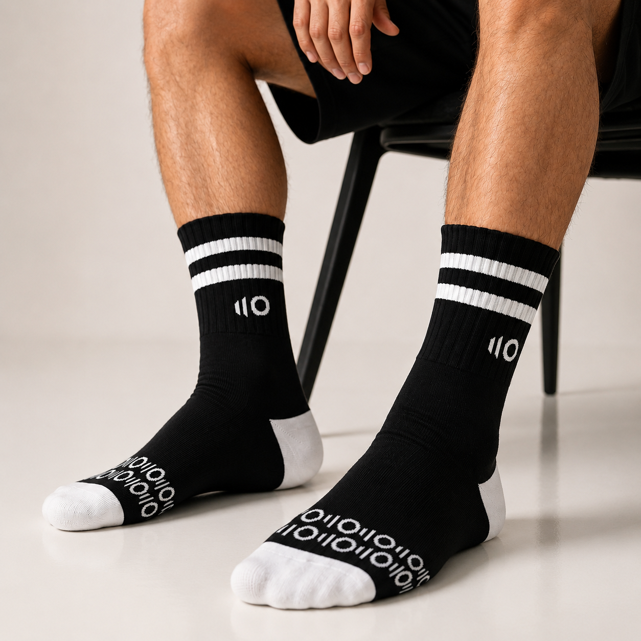 Black socks with white stripes and Eleven Zero logo worn by a person sitting on a chair.