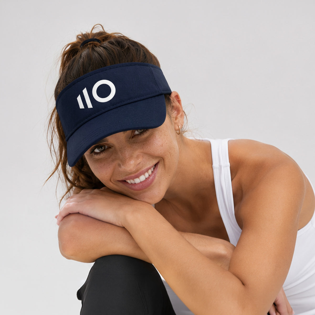 Woman wearing a navy visor with a logo on a light gray background